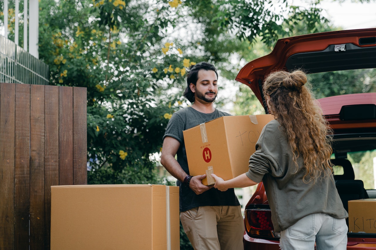 Two friends carrying moving boxes to a car
