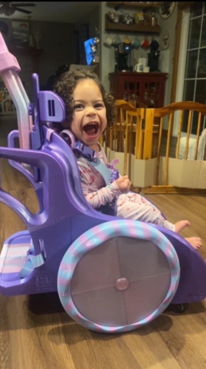 A toddler laughing in her purple Toddler Mobility Trainer at home